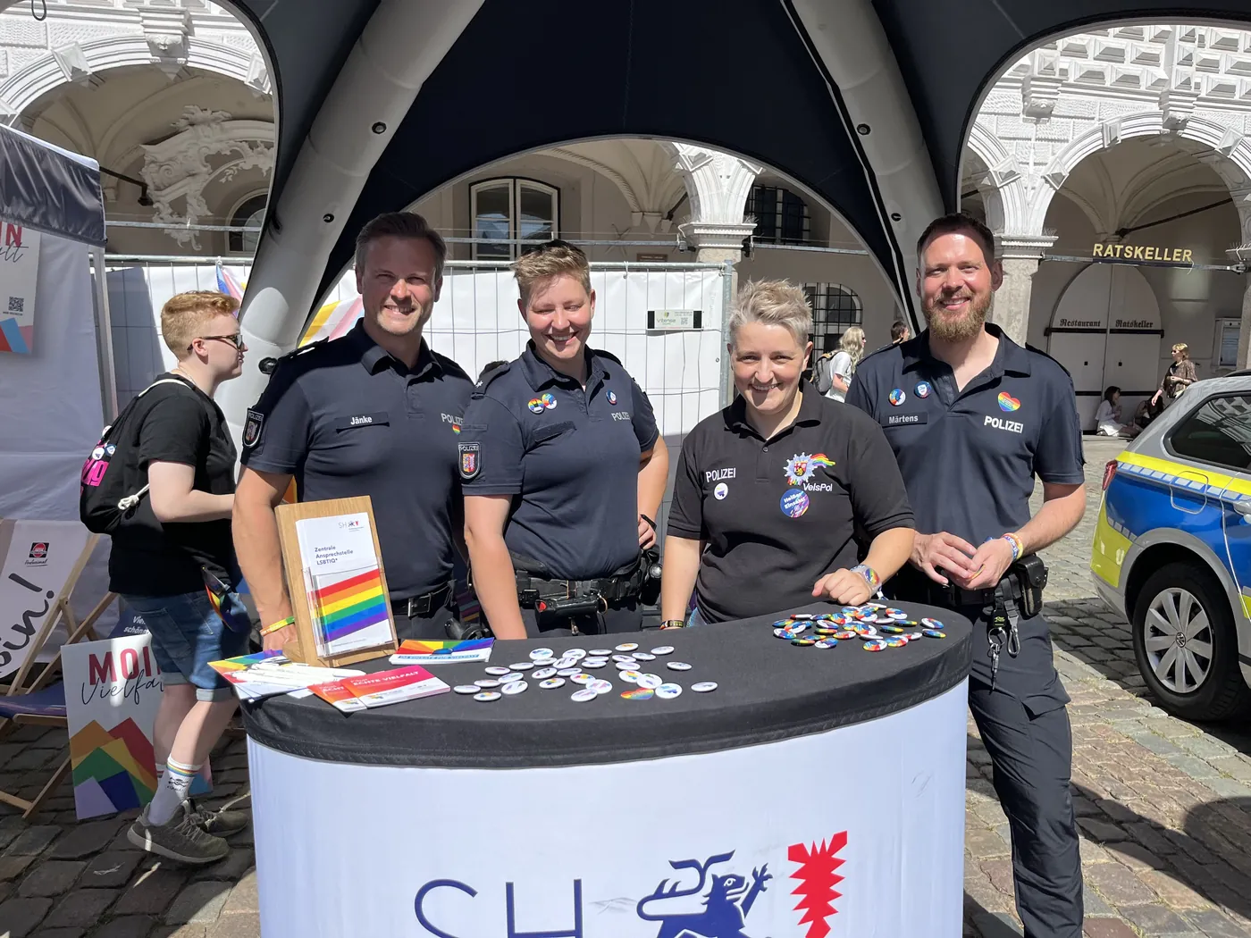 Vier Polizeibedienstete am Stand der Zentralen Ansprechstelle LSBTIQ* der Landespolizei Schleswig-Holstein, auf dem Tisch Buttons und Informationsmaterial.