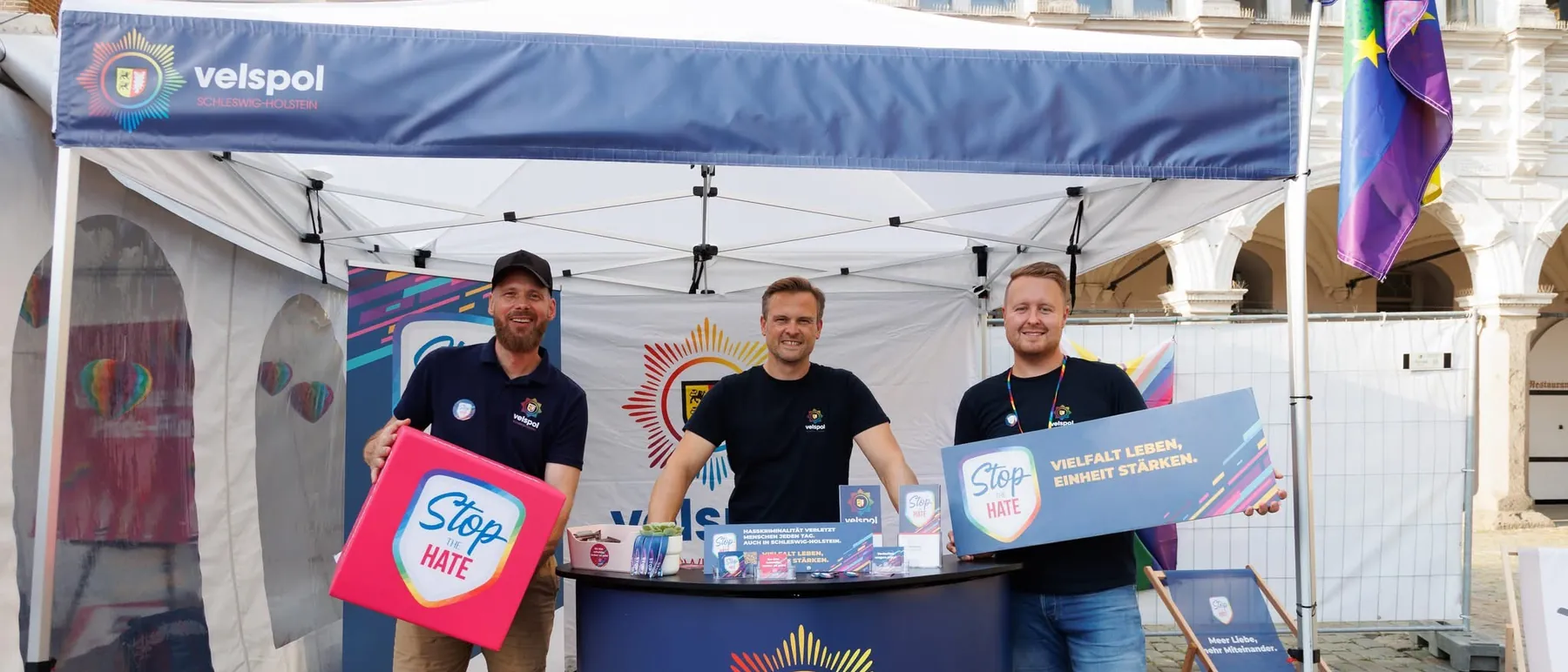 Drei Mitglieder von velspol Schleswig-Holstein am Infostand vor dem Lübecker Rathaus, mit STOP-the-HATE-Schildern in den Händen.